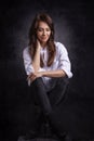 Studio portrait of a brunette haired attractive woman wearing white shirt and black jeans while posing at isolated dark background Royalty Free Stock Photo