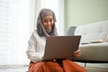 Attractive Asian Muslim woman wearing hijab, using notebook laptop in her living room Royalty Free Stock Photo