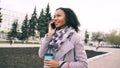 Attractive mixed race girl talking smartphone and drinking coffee walks in city street with bags. Young woman walking Royalty Free Stock Photo