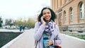 Attractive mixed race girl talking smartphone and drinking coffee walks in city street with bags. Young woman walking Royalty Free Stock Photo