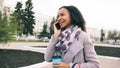 Attractive mixed race girl talking smartphone and drinking coffee walks in city street with bags. Young woman walking Royalty Free Stock Photo