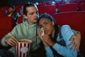 Attractive mixed race young woman crying, looking emotional while watching movie together with her boyfriend, sitting in Royalty Free Stock Photo