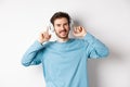 Attractive modern man with beard, smiling pleased, touching headphone on head while listening to music, standing over Royalty Free Stock Photo