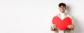 Attractive modern man smiling and looking at camera hopeful, holding big red Valentines heart, waiting for soulmate on Royalty Free Stock Photo
