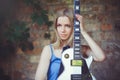 Attractive modest young blond woman with a white guitar in hand holding a wall background shy and inquisitive