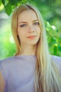 Attractive modest young girl with blond hair and natural make-up in purple dress outdoors, tenderness and softness on nature