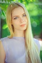 Attractive modest young girl with blond hair and natural make-up in purple dress outdoors, tenderness and softness on nature