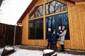 Attractive mother with her kids in winter day stand near wooden house with large window Royalty Free Stock Photo