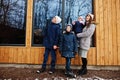 Attractive mother with her kids in winter day stand near wooden house with large window Royalty Free Stock Photo