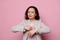 Attractive confident multi-ethnic businesswoman, showing you time on her wristwatch, looking at camera, pink background Royalty Free Stock Photo