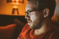 Attractive nerdy man with glasses is working late night on the computer in living room in home office