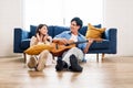 Attractive new marriage man and woman sit on the floor enjoy singing and playing guitar in the living room at the new home.