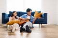 Attractive new marriage man and woman sit on the floor enjoy singing and playing guitar in the living room at the new home.