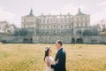 Attractive newlywed couple embracing at green sunny lawn near beautiful ruined baroque palace. Loving groom holding Royalty Free Stock Photo