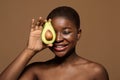 Attractive Nude Black Female With Clean Skin Covering Eye With Avocado Half