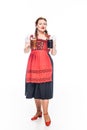 attractive oktoberfest waitress in traditional bavarian dress showing mugs with light and dark beer Royalty Free Stock Photo