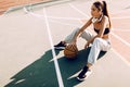 Attractive athletic young woman outdoor posing sitting on basketball court holding basketball Royalty Free Stock Photo