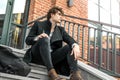 Attractive pensive man sitting on steps on red bricked building background. Royalty Free Stock Photo