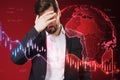 Attractive pensive young european businessman with glowing falling red forex chart and globe on blurry background. Global economy