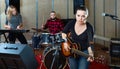 Attractive female soloist playing guitar and singing with her music band in sound studio Royalty Free Stock Photo