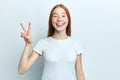 Attractive positive girl with freckles is showing peace sign and smiling.