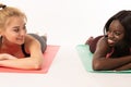 Attractive positive international girls lying on the yoga mats and looking at each other while relaxing between