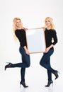 Attractive positive young blonde sisters twins posing with blank board Royalty Free Stock Photo