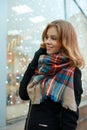 Attractive positive young woman with a wonderful smile in a winter black coat in stylish gloves with a woolen fashion scarf