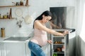 Pregnant woman looking into opened fridge in kitchen Royalty Free Stock Photo