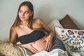 Attractive pregnant woman is sitting in bed and holding her belly. Last months of pregnancy. Royalty Free Stock Photo