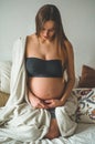 Attractive pregnant woman is sitting in bed and holding her belly. Last months of pregnancy. Royalty Free Stock Photo