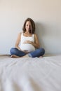 Attractive pregnant woman is sitting in bed, holding her belly and smiling. Last months of pregnancy.Lifestyle indoors Royalty Free Stock Photo