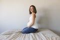 Attractive pregnant woman is sitting in bed, holding her belly and smiling. Last months of pregnancy.Lifestyle indoors Royalty Free Stock Photo