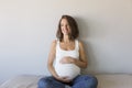 Attractive pregnant woman is sitting in bed, holding her belly and smiling. Last months of pregnancy.Lifestyle indoors Royalty Free Stock Photo