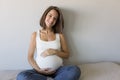 Attractive pregnant woman is sitting in bed, holding her belly and smiling. Last months of pregnancy.Lifestyle indoors Royalty Free Stock Photo