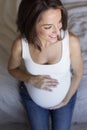 Attractive pregnant woman is sitting in bed, holding her belly and smiling. Last months of pregnancy.Lifestyle indoors Royalty Free Stock Photo