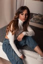 Attractive pretty young woman with long red hair in stylish clothes sits on the bed and looks down. Beautiful European girl Royalty Free Stock Photo