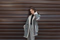 Attractive pretty young woman in trendy black T-shirt in a vintage checkered coat in gray stylish pants poses near a metal wall