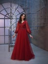 Attractive princess locked in tower, dressed in a luxurious red expensive long royal dress, her dark hair lies in waves