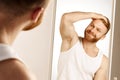 Attractive red haired, bearded man touching face applying moisturizer on face, standing near mirror in bathroom. Male Royalty Free Stock Photo