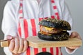 An attractive red-haired boy is holding a wooden chopping Board with a hamburger. Recipe for cooking black cheeseberger Royalty Free Stock Photo