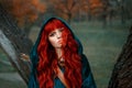 Attractive red-haired girl looking at the camera with brown eyes, wearing blue velor velvet cloak with hood on her head