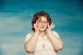 Attractive red-haired plump woman in a white suit adjusts red glasses on a blue background Royalty Free Stock Photo