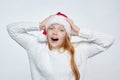 Attractive red-haired teenage girl wearing Santa hat. she holds her head in her hands in amazement. photo session in the studio on Royalty Free Stock Photo
