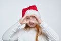 Attractive red-haired teenage girl wearing Santa hat. she looks through binoculars folded from her fingers. Christmas and New Year Royalty Free Stock Photo