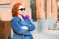 Attractive red-haired woman in a blue coat and jeans stands outside a brick building facade Royalty Free Stock Photo