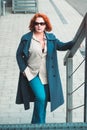 Attractive red-haired woman in a blue coat and sunglasses climbs the metal stairs Royalty Free Stock Photo