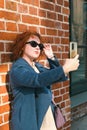 Attractive red-haired woman in a blue coat takes a selfie on smartphone Royalty Free Stock Photo