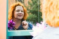 Attractive red-haired woman looks at her reflection in a mirrored window and smiles