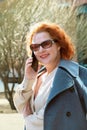 Attractive red-haired woman in an oversized shirt and a blue coat is talking on a mobile phone Royalty Free Stock Photo